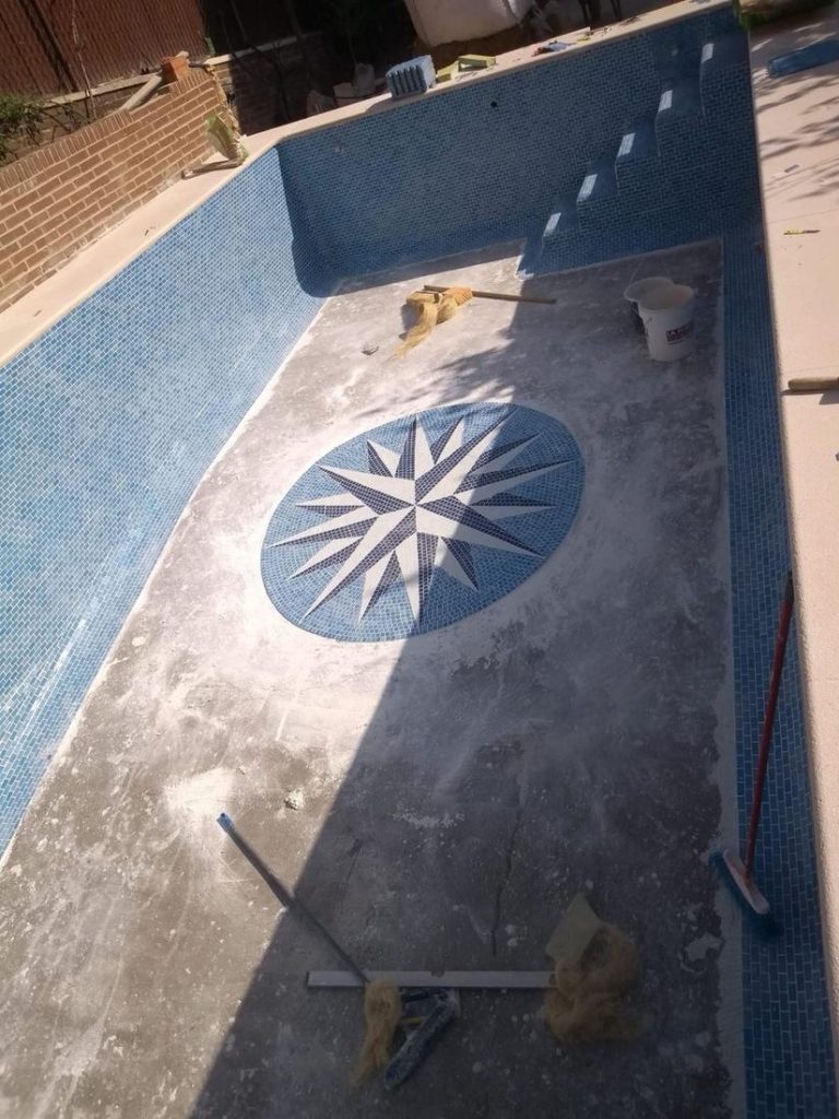 Vaso de piscina en obra con el mosaico de rosa de los vientos ya colocado y el gresite azul a medio revestir