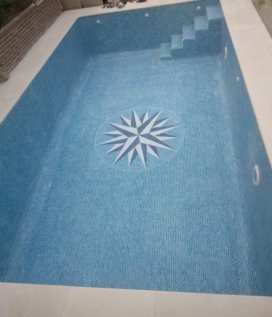 La misma piscina terminada, revestida por completo con gresite azul y el mosaico de rosa de los vientos en el fondo