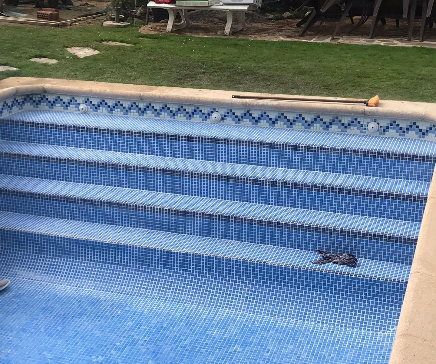 Escalera de piscina revestida con gresite azul y cenefa decorativa, durante los trabajos