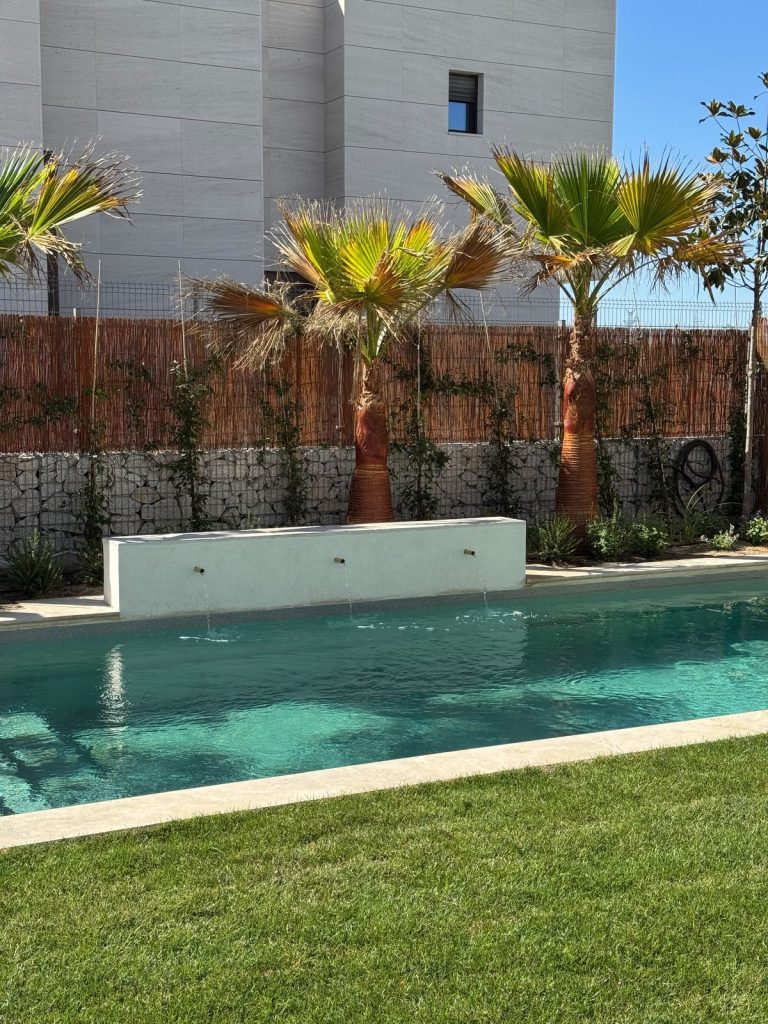 Piscina desbordante con lamina de agua sobre un muro y palmeras al fondo
