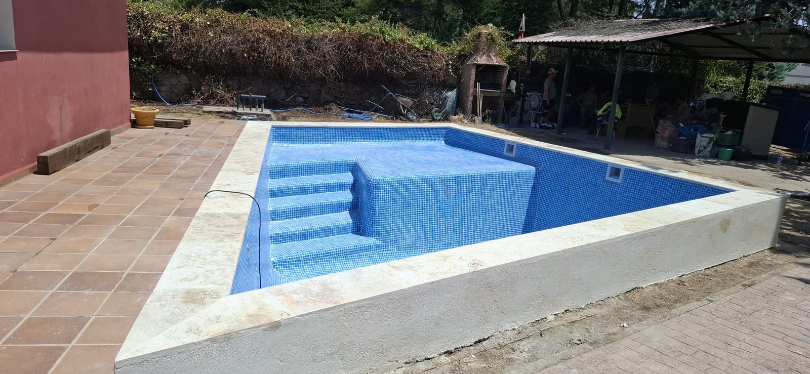 Piscina terminada con gresite azul y escalones de obra con cenefa marcando el borde de cada peldaño