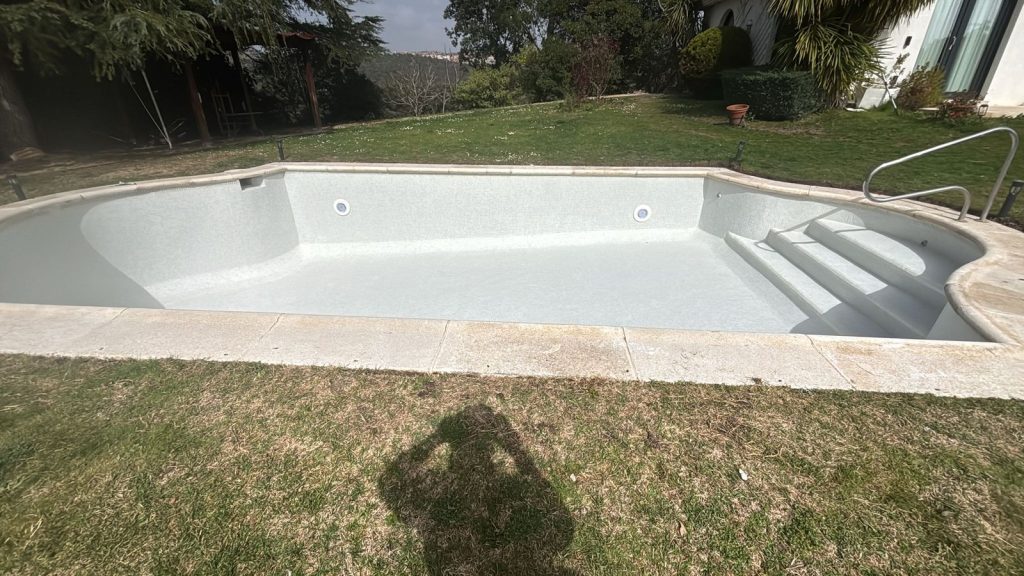 Piscina de forma libre terminada, con el revestimiento claro y los focos ya instalados en el vaso