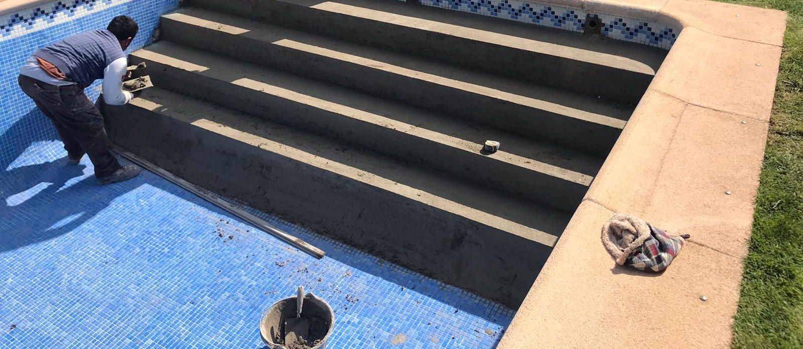 Escalera de piscina terminada tras la reforma, con los peldaños rematados y la cenefa de gresite colocada