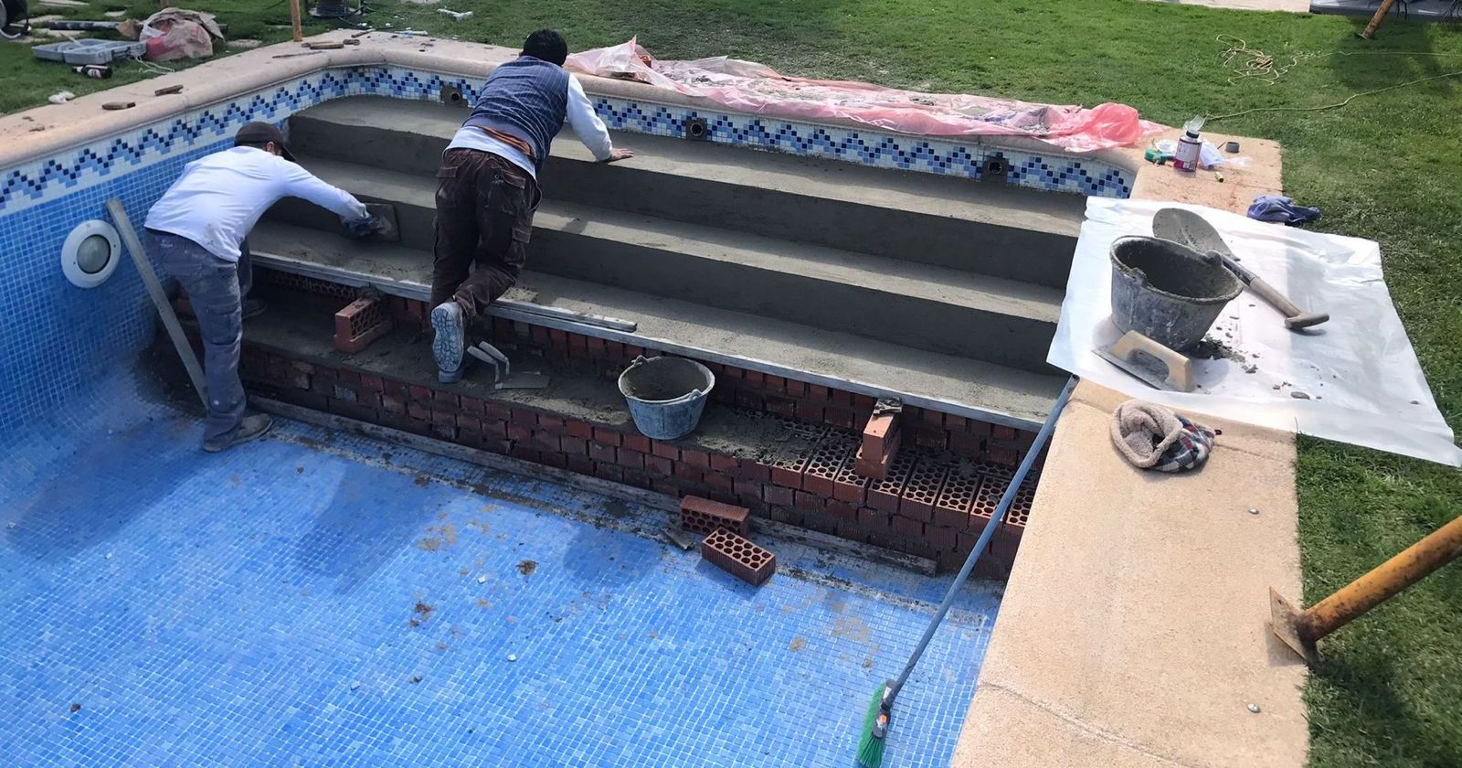 Operario colocando gresite sobre los peldaños de una escalera de piscina en reforma